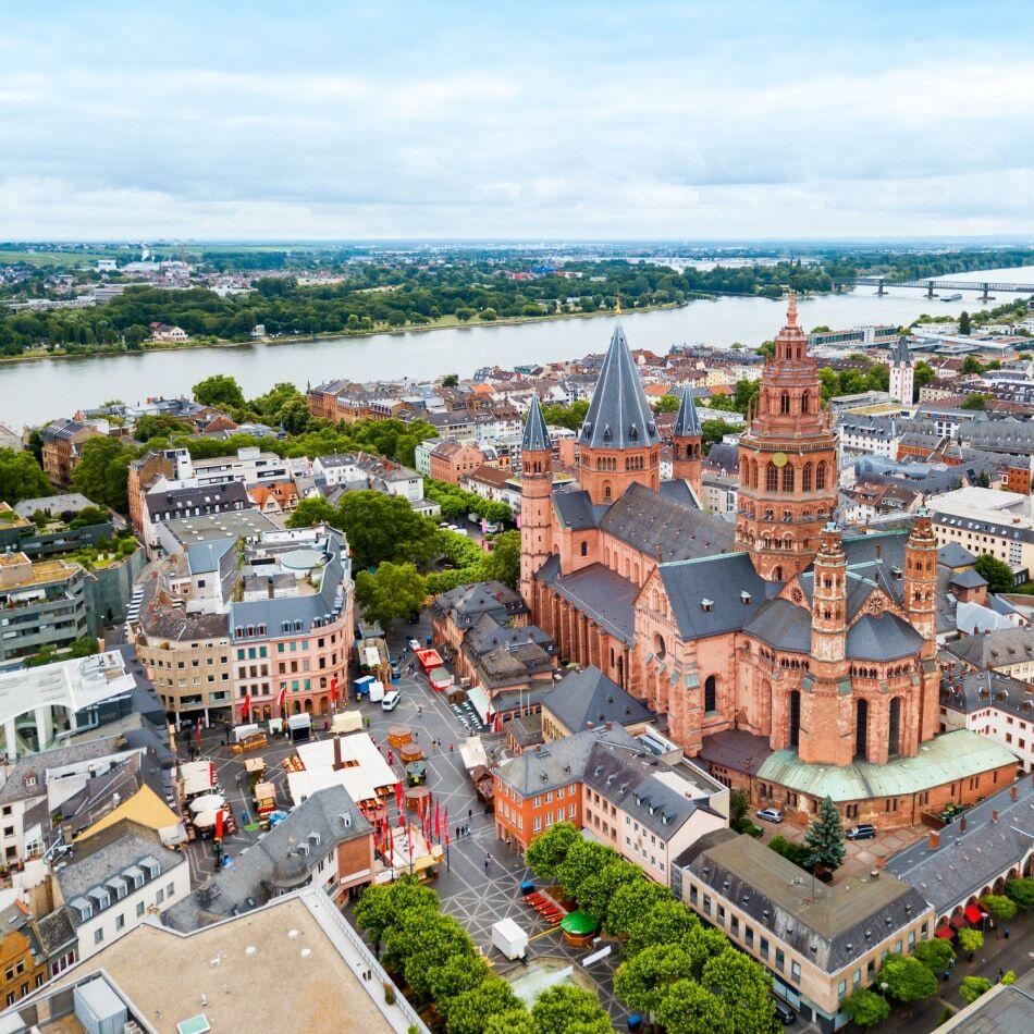 Luftaufnahme des Mainzer Doms (St. Martin) mit Blick auf die Altstadt von Mainz und den Rhein im Hintergrund. Die Aufnahme zeigt eindrucksvoll die architektonische Schönheit der historischen Innenstadt von Mainz aus der Vogelperspektive.