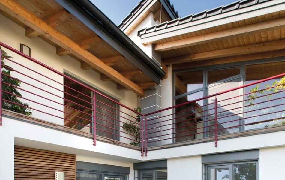 Modernes Wohnhaus mit großem Balkon, Holzüberdachung und roten Metallgeländern. Große Fensterfronten sorgen für viel Tageslicht